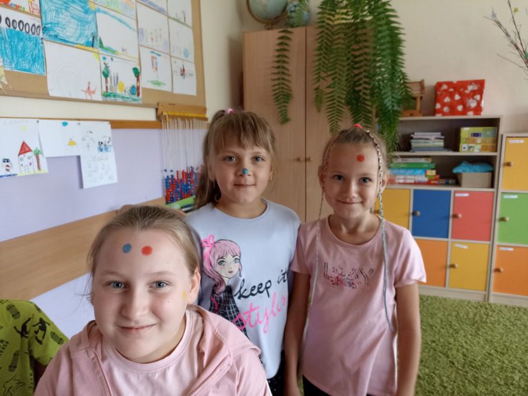 W sali lekcyjnej stoją trzy dziewczynki z pomalowanymi w kropki twarzami