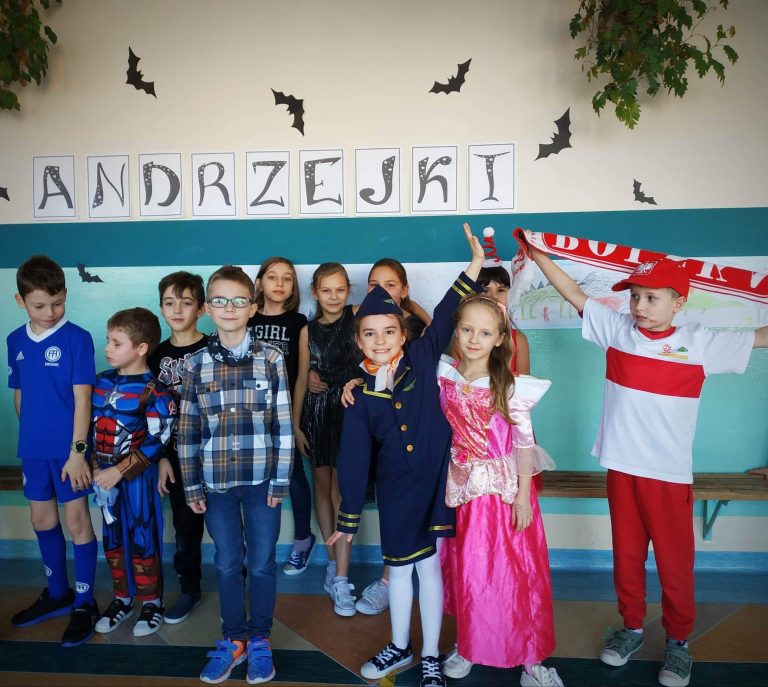 Grupa dzieci w przebraniach - m.in. księżniczki, piłkarza czy marynarza stoi na tle napisu Andrzejki.