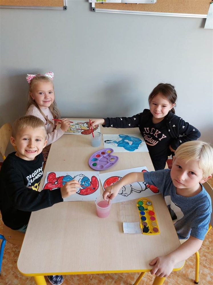Czworo dzieci maluje farbami przy stoliku.