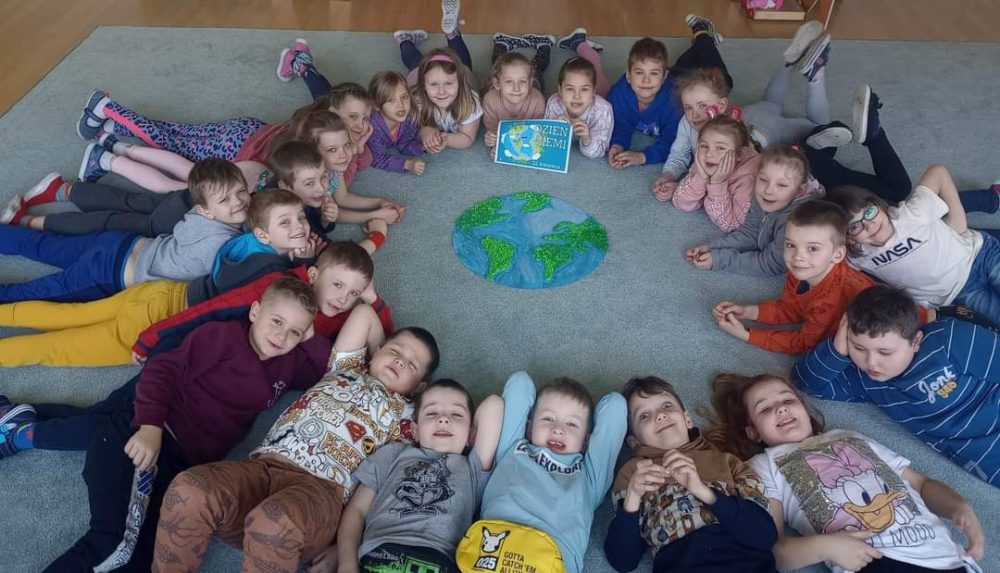 Grupa dzieci leżących na dywanie a pośród nich makieta Ziemi.