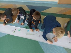 Kilkoro dzieci siedzi na podłodze i maluje wspólnie na kartce papieru.