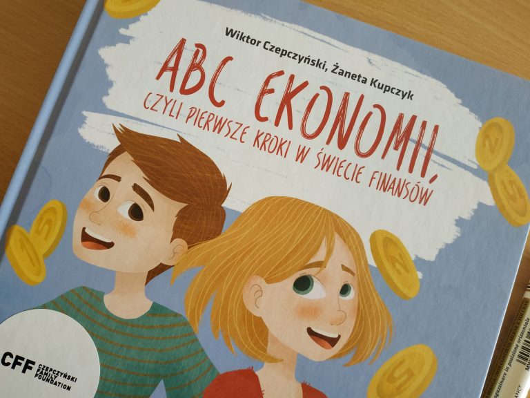 Zdjęcie przedstawia okładkę książki „ABC EKONOMII, czyli pierwsze kroki w świecie finansów”, na której znajdują się uśmiechnięty chłopiec i dziewczynka oraz monety.