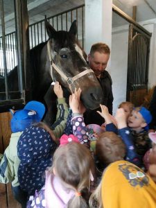 Grupa dzieci głaszcze konia, którego trzyma właściciel.
