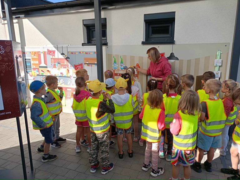 Grupa dzieci ogląda tablice edukacyjne i słucha przewodnika.