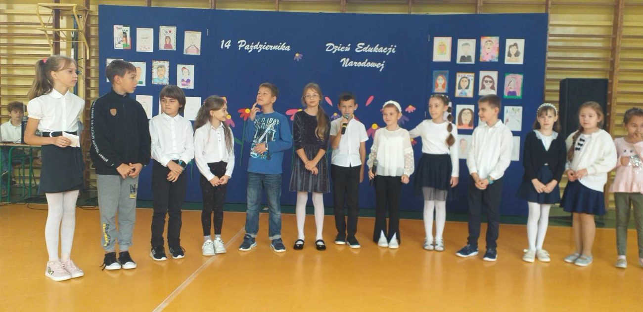 Na zdjęciu nr 2 uczniowie klas młodszych – III i IV – ubrani galowo na tle niebieskiej dekoracji. W tle napis: „14 października Dzień Edukacji Narodowej”.