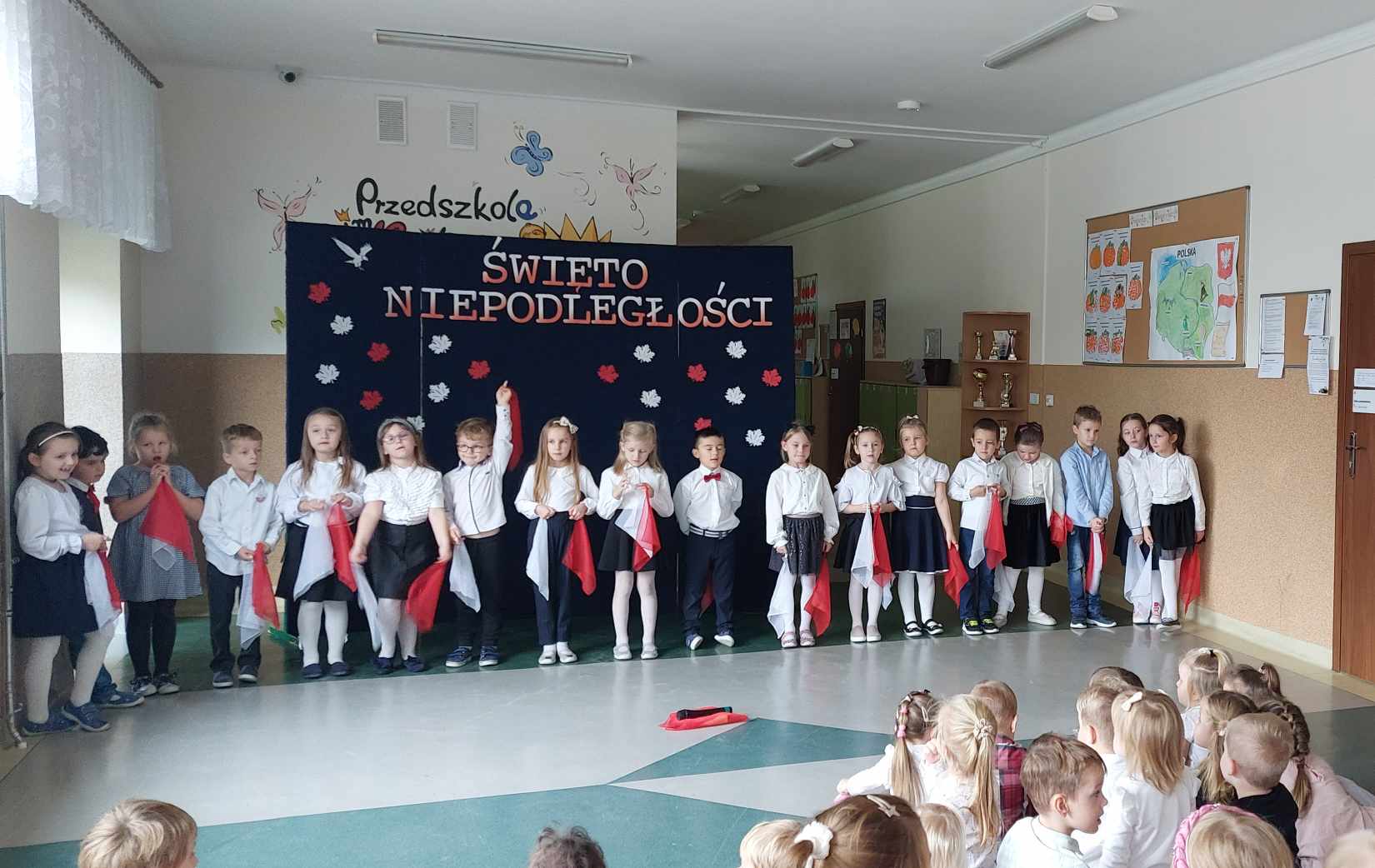 Dzieci z grupy Odkrywców są elegancko ubrane i występują podczas apelu. W tle widać tablicę z napisem "Święto Niepodległości". Na pierwszym planie widać widownię.