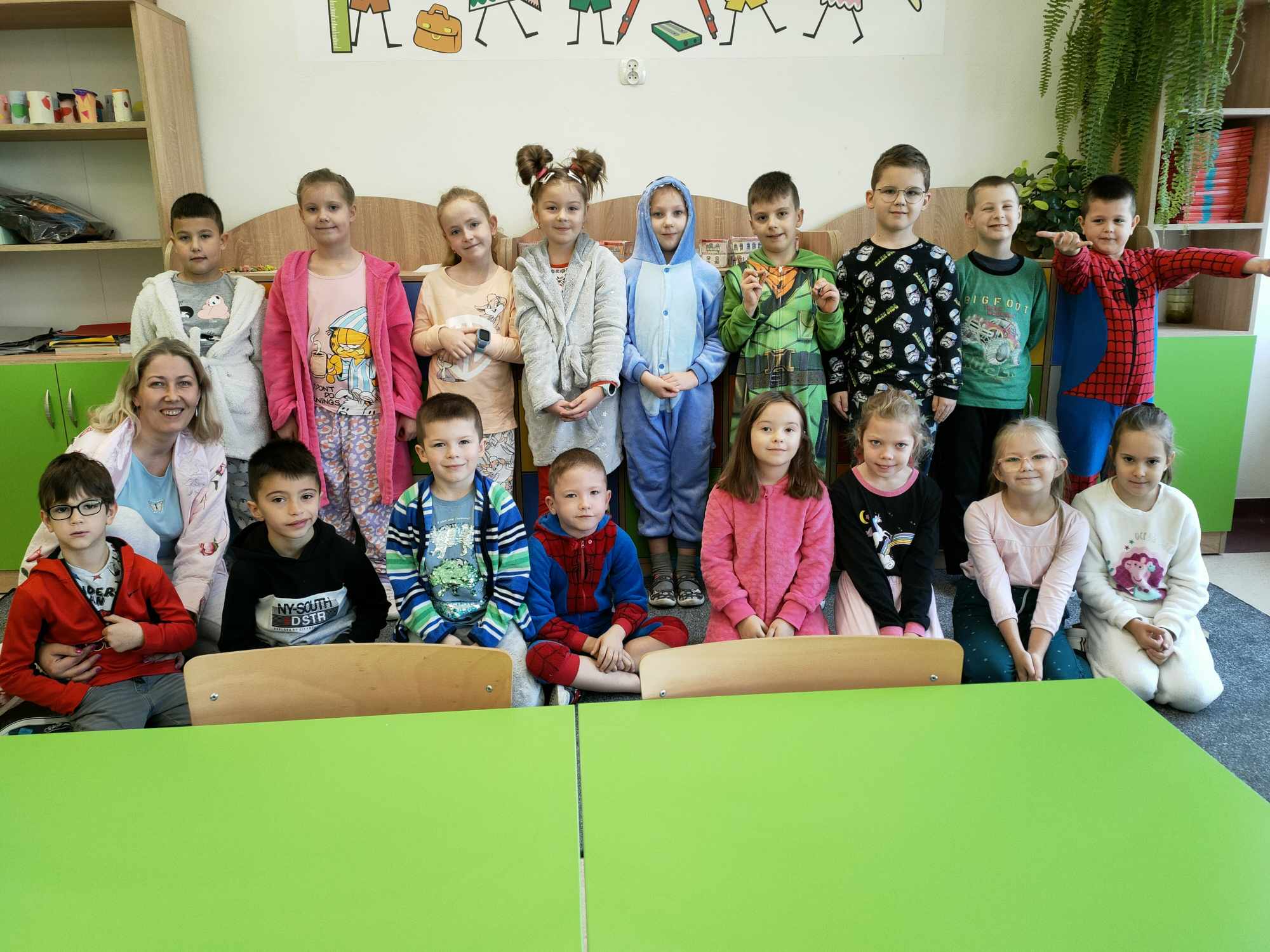 Grupa dzieci w piżamach w towarzystwie wychowawczyni pozuje do zdjęcia.