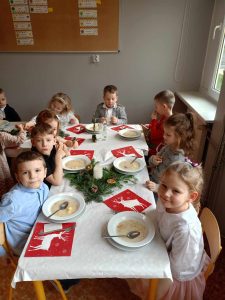Grupa Tropiciele siedzi przy stole podczas uroczystego obiadu - Wigilii przedszkolnej.