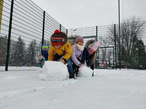 Na zdjęciu znajdują się uczniowie, którzy wspólnie lepią bałwana.