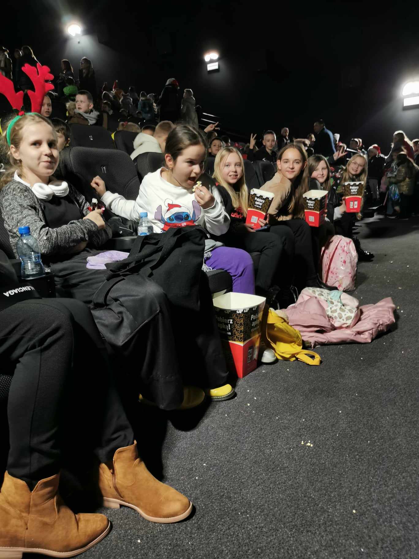 Na zdjęciu widać 6 dziewczynek, które siedzą w pierwszym rzędzie w sali kinowej. W tle widać pozostałych widzów kina.