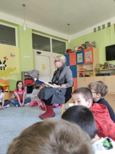 Pani poetka czyta dzieciom bajkę. Przedszkolaki słuchają siedząc na dywanie.