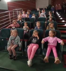 Grupa dzieci siedzi na widowni i ogląda spektakl.