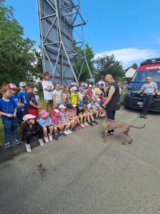 Grupa dzieci słucha jak ratownik trenuje pasa. W tle widać wóz ratunkowy i ratownika.