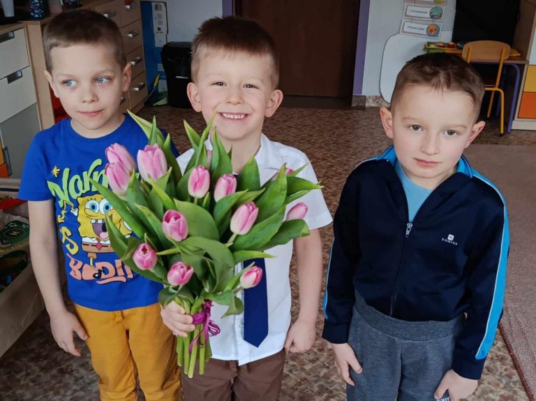 Trzech chłopców wręcza kwiaty swojej pani.