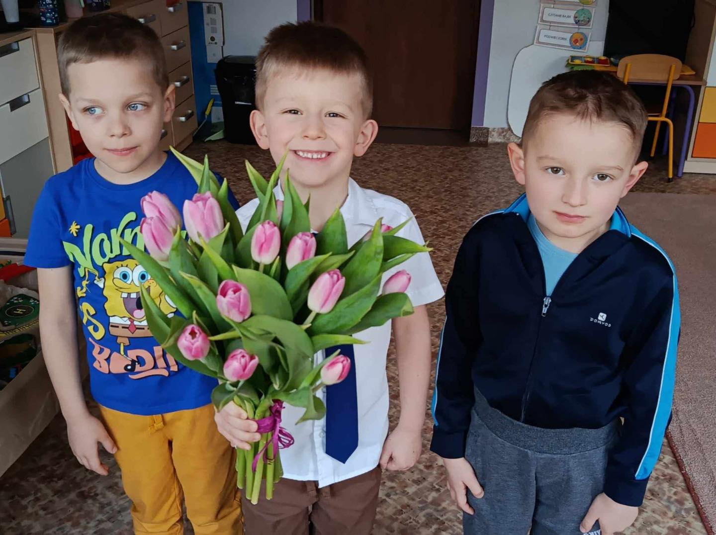 Trzech chłopców wręcza kwiaty swojej pani.