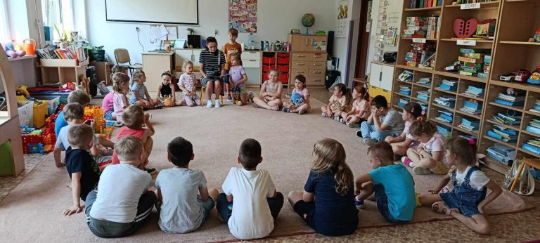 Grupa dzieci siedzi na dywanie i słucha bajki czytanej przez jedną z mam.