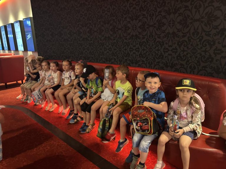 Grupa dzieci siedzi na ławce przed wejście do kina.