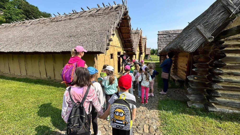 Grupa dzieci wraz z nauczycielami zwiedza skansen.