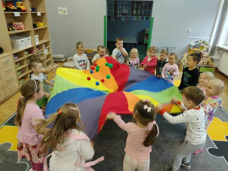 Grupa dzieci bawi się chustą animacyjną - nad środkiem chusty unoszą się piłeczki.