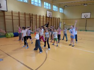Grupa przedszkolaków ćwiczy na sali gimnstycznej.