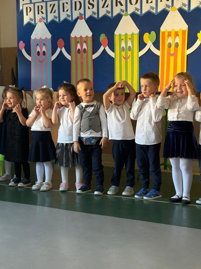 Grupa dzieci występuje podczas pasowania. Z tyłu widać dekorację.