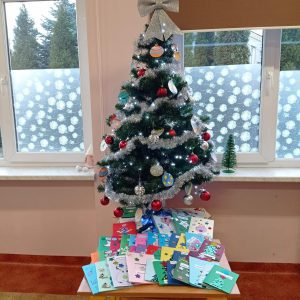Choinka jest bogato ozdobiona a pod nią leżą kartki przygotowane przez dzieci.
