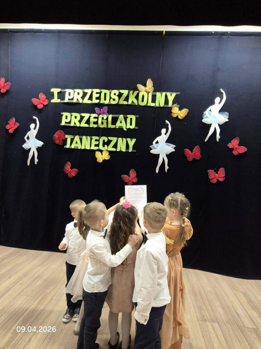 Dzieci oglądają dyplom. W tle widać dekorację i nazwę konkursu.